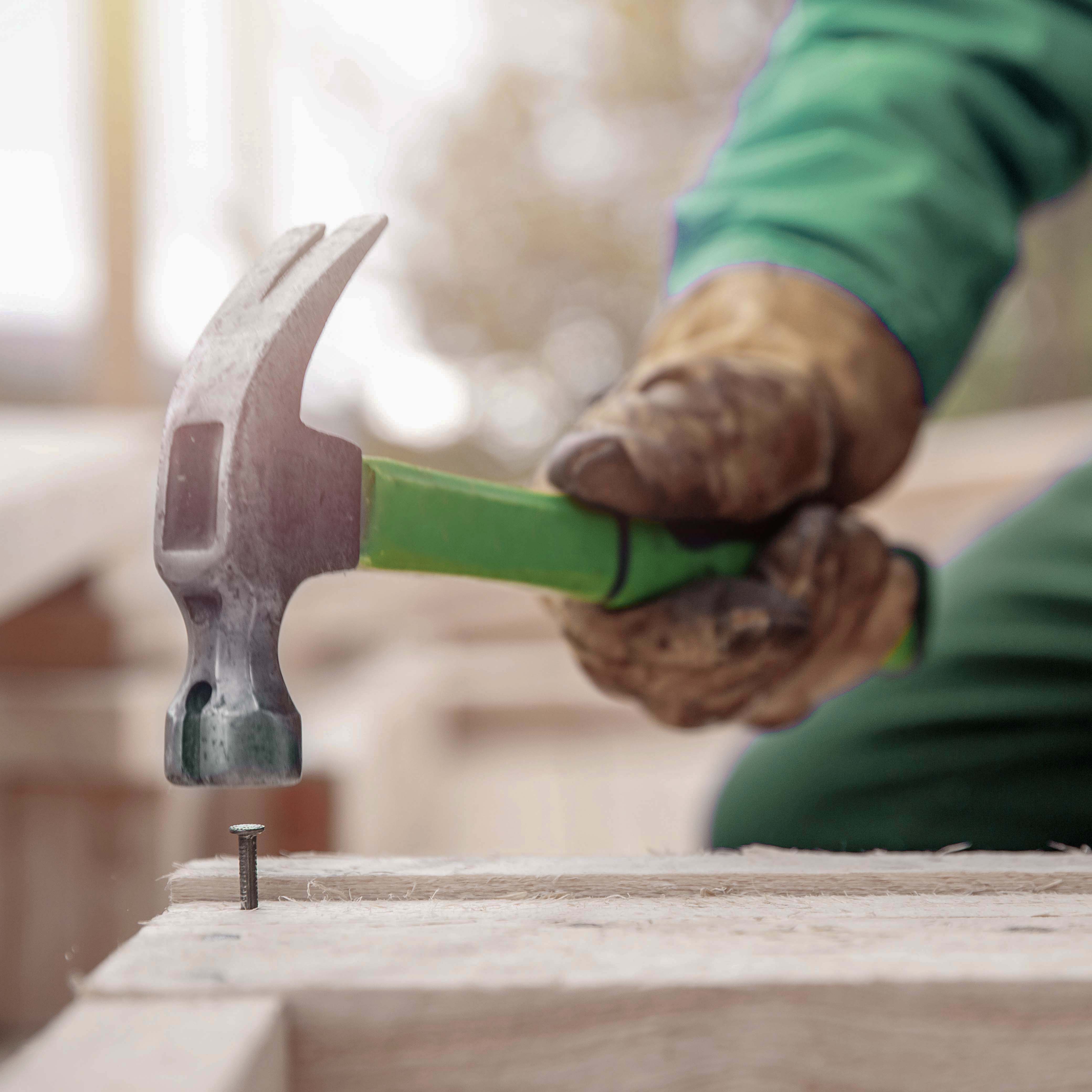 Person schlägt Nagel mit einem Hammer in Holz